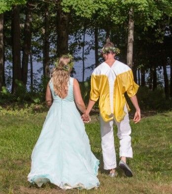 A bride and groom are walking through a field holding hands.