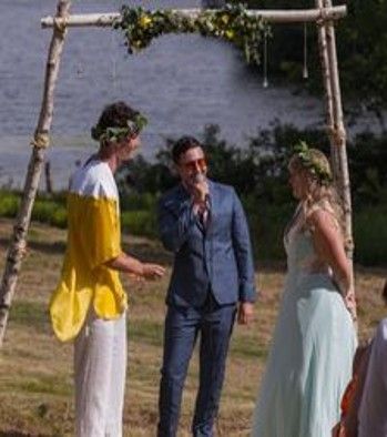 A bride and groom are standing under a wooden arch at their wedding ceremony.