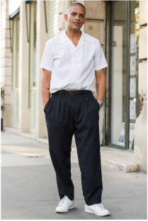 A man wearing a white shirt and black pants is standing with his hands in his pockets