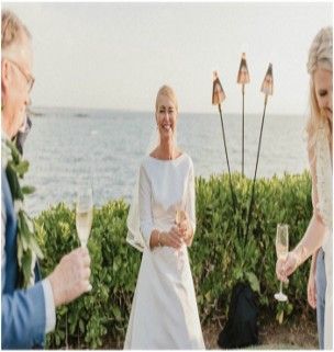 A bride and groom are toasting with champagne in front of the ocean.