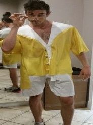 A man in a yellow shirt and white shorts is standing in front of a mirror.