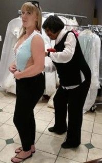 A woman is helping a woman try on a wedding dress.