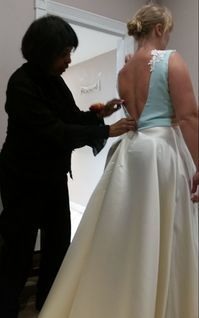 A woman is helping a woman try on a wedding dress.