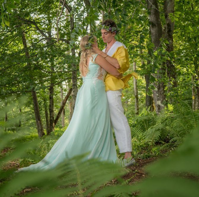 A man in a yellow jacket and a woman in a blue dress are standing in the woods.
