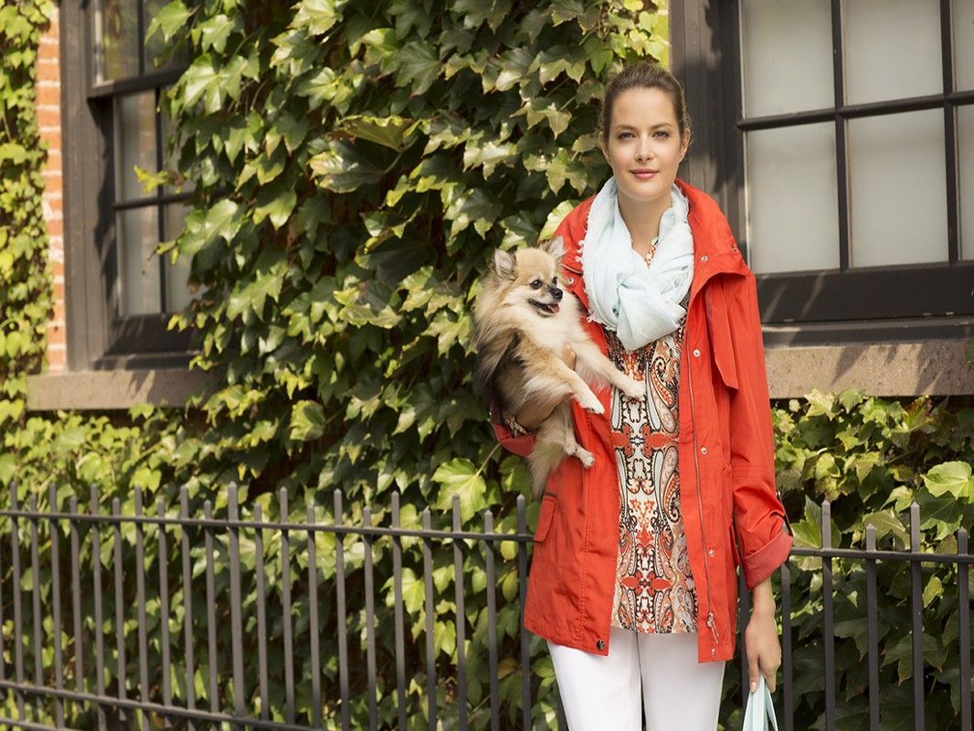 A woman in a red jacket is holding a small dog in her arms.