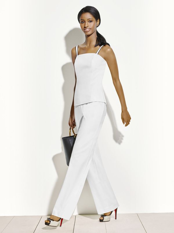 A woman in a white top and pants is walking with a black purse