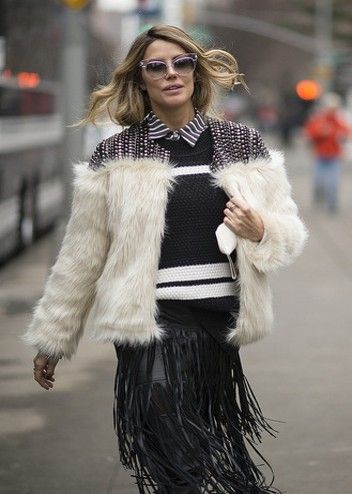 A woman wearing a fur coat and fringe skirt is walking down the street.