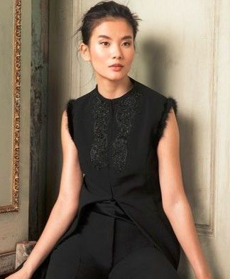 A woman in a black dress is sitting on a chair.