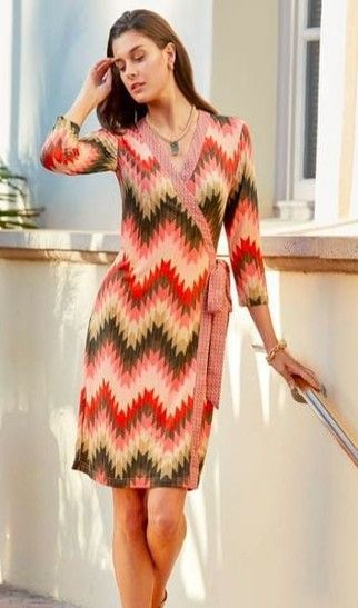 A woman in a wrap dress is standing next to a railing.