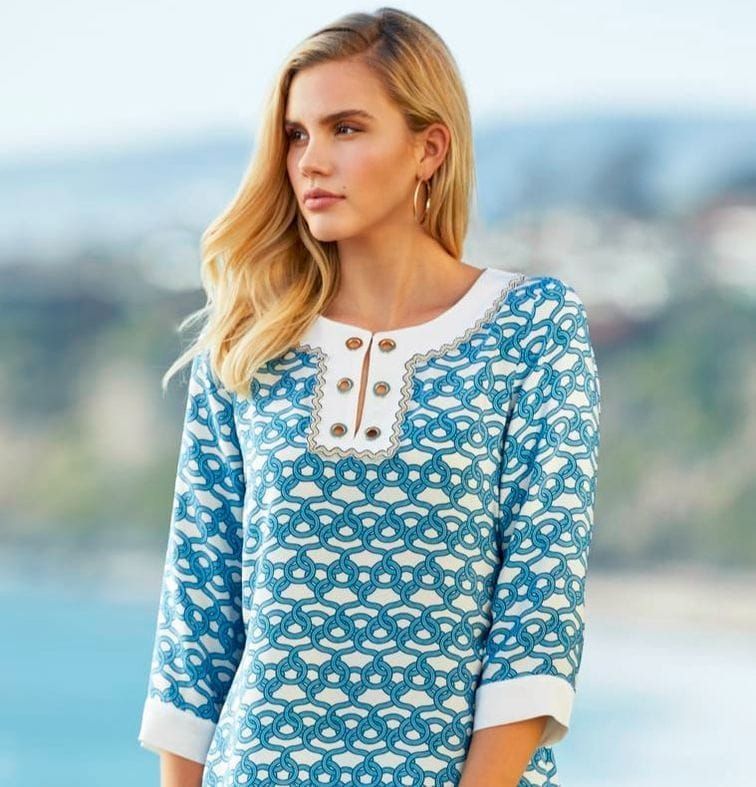 A woman wearing a blue and white sweater is standing in front of a body of water.
