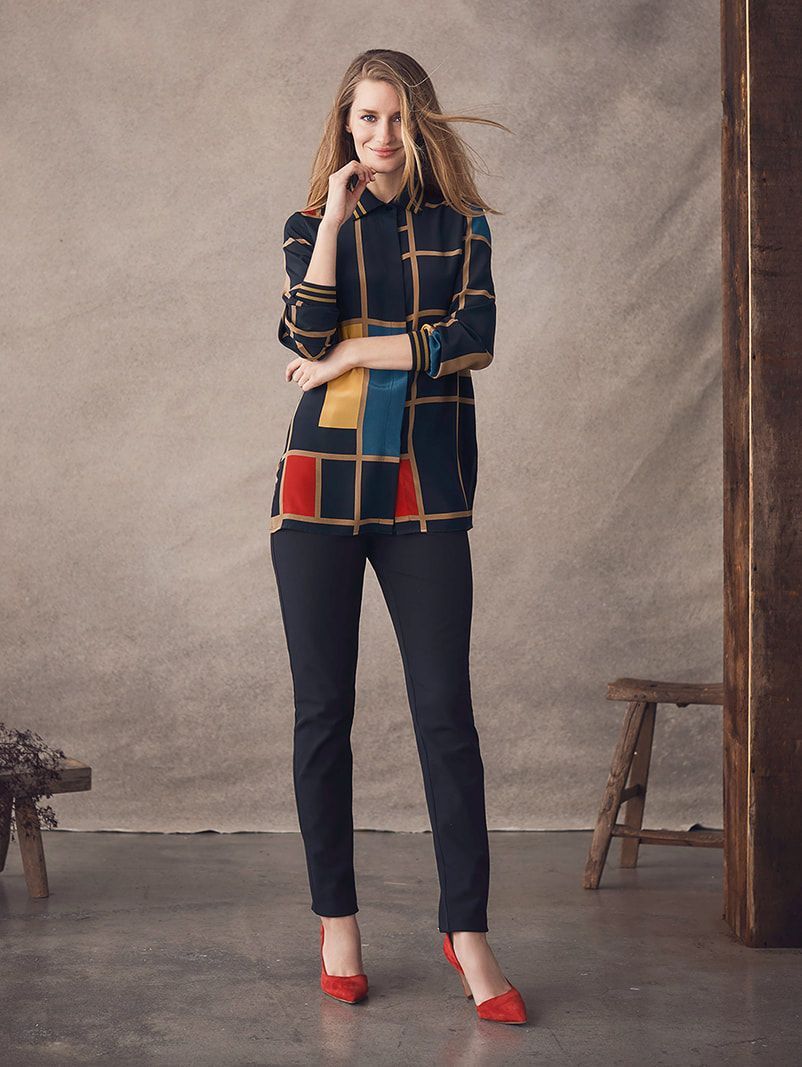 A woman wearing a plaid shirt and black pants is standing in front of a wall.
