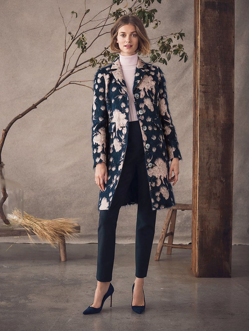 A woman is wearing a floral coat and black pants.