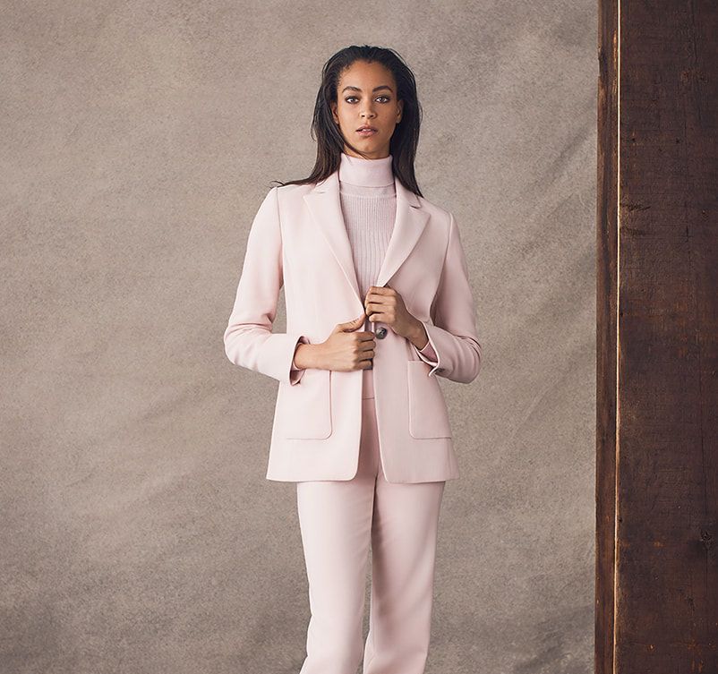 A woman in a pink suit is standing in front of a wall