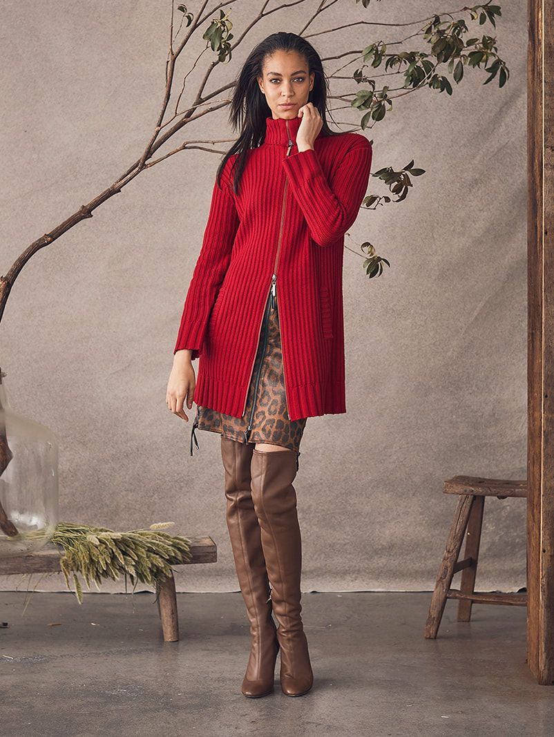 A woman is wearing a red sweater and brown over the knee boots.
