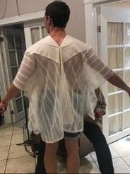 A man is standing in a room wearing a white sheer shirt.