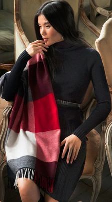 A woman wearing a black dress and a red and white scarf is sitting on a chair.