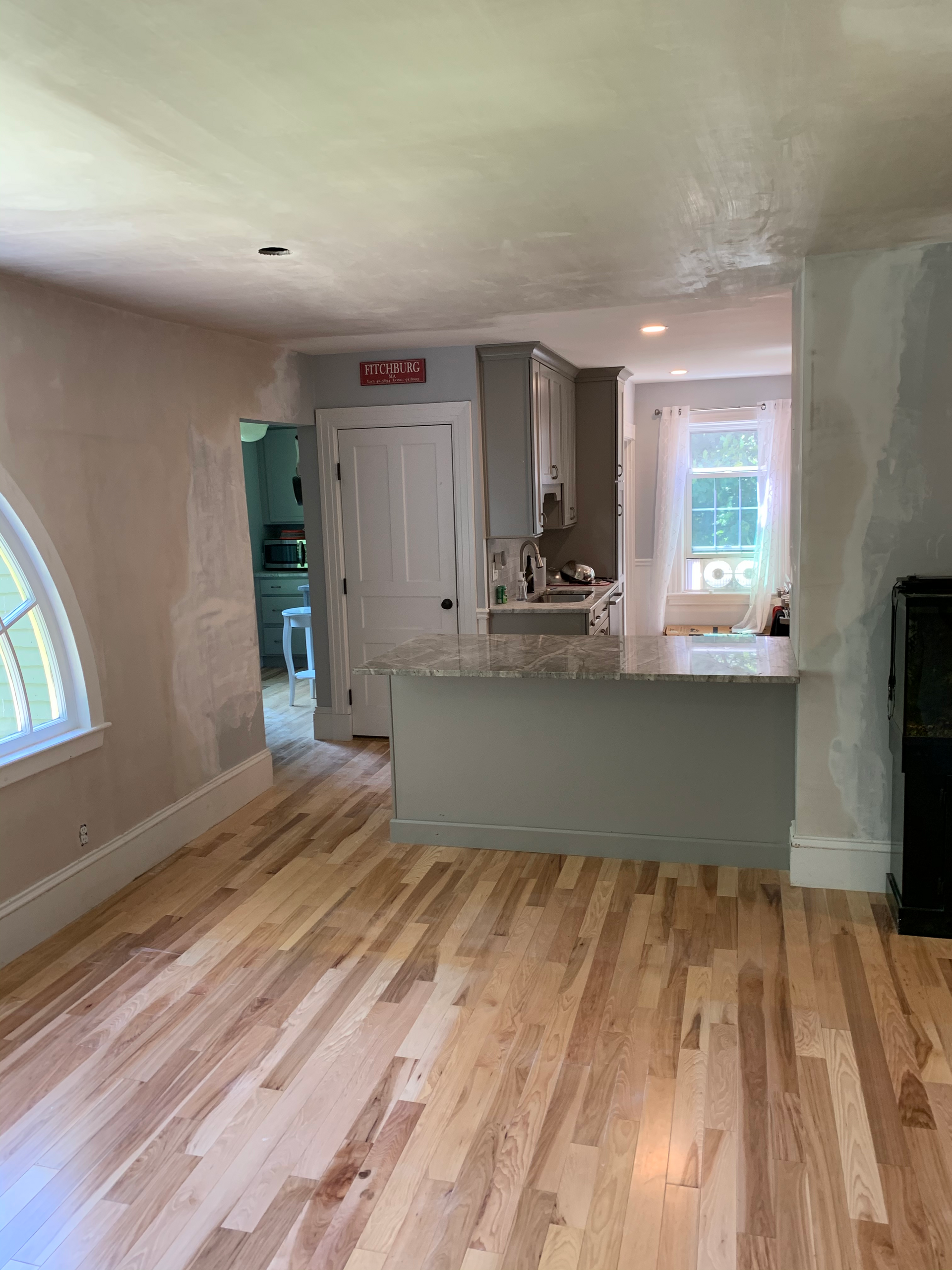 A living room with hardwood floors and a kitchen in the background.