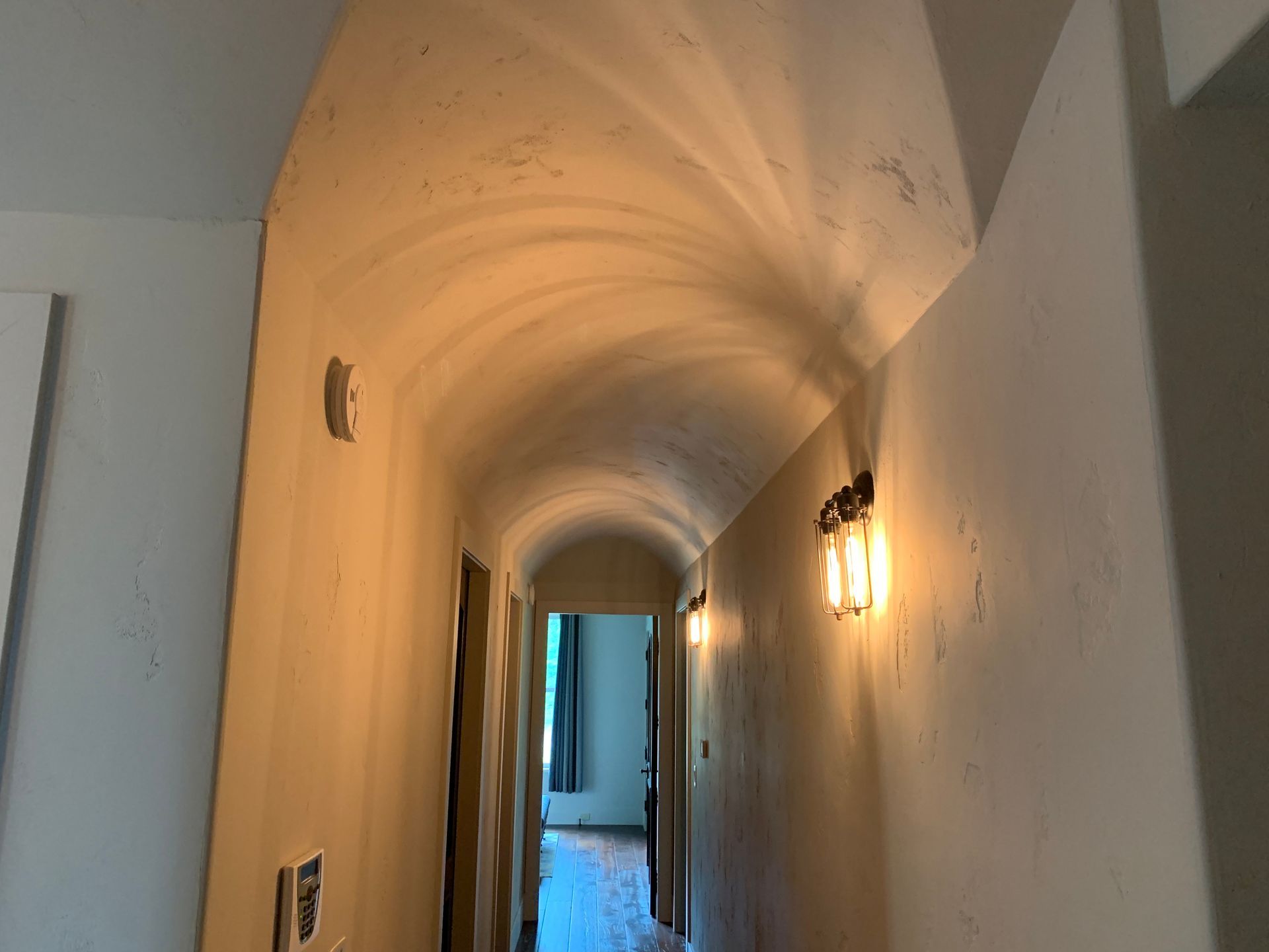 A long hallway with a curved ceiling and a light on the wall.