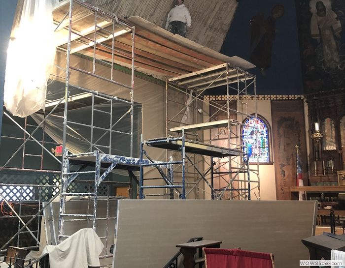 A man is standing on top of a scaffolding in a church.
