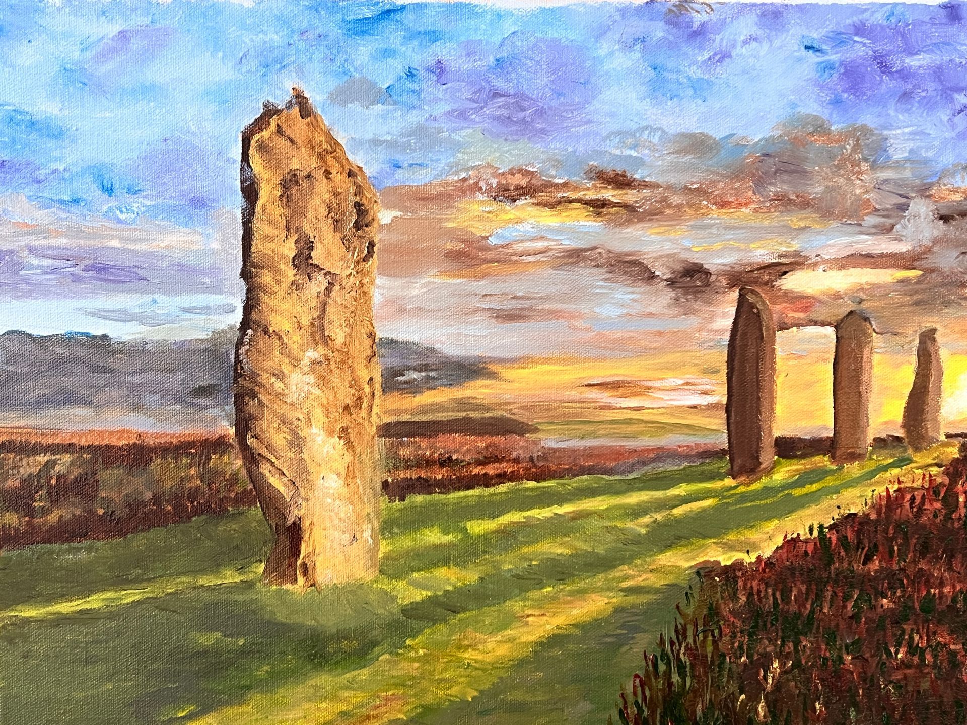 Standing stones in a field at sunset, with warm hues of orange and gold in the sky.