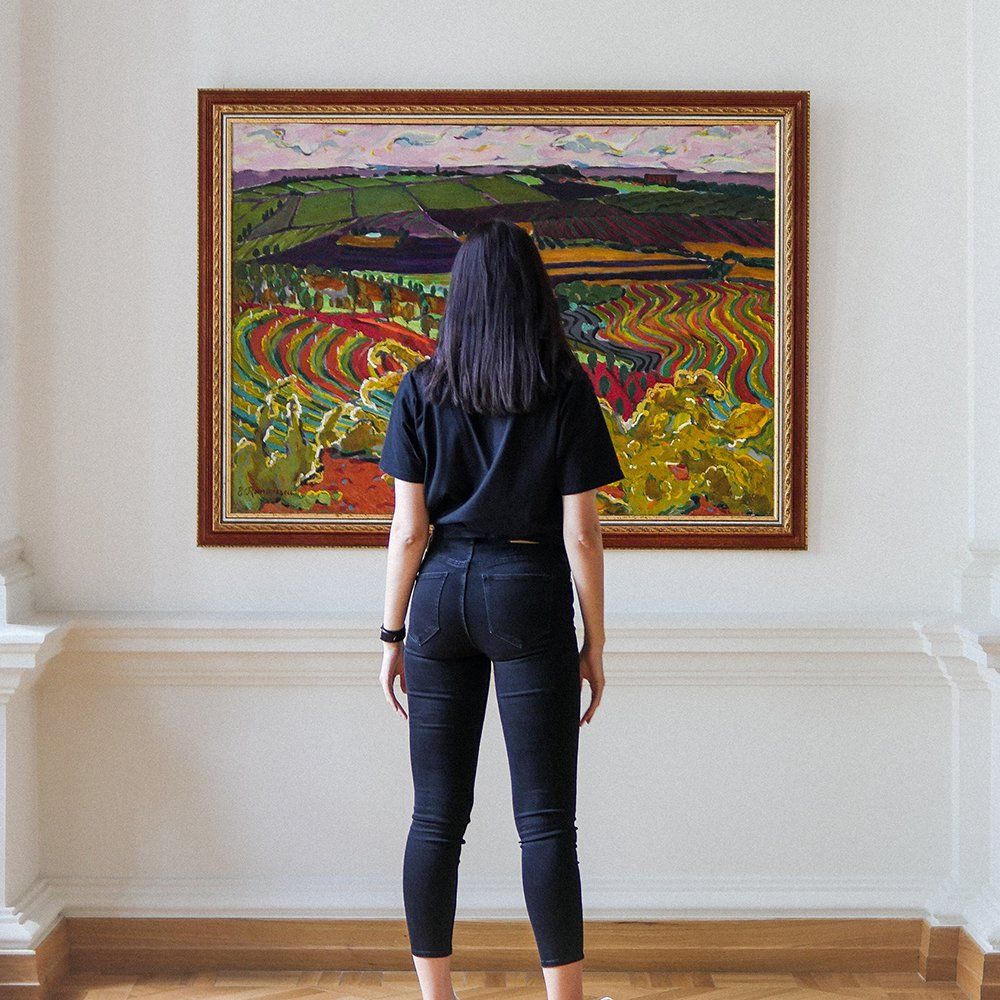Woman in black clothing gazes at landscape painting in a gallery.