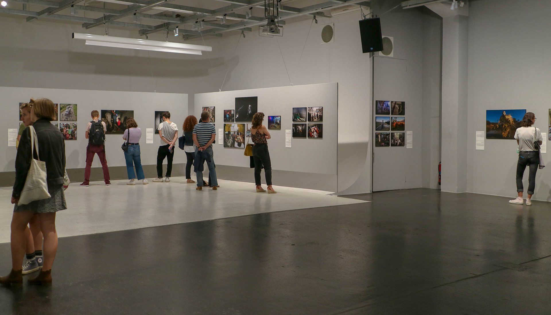 People viewing photographs in an art gallery. White walls, dark floor, and overhead lighting.