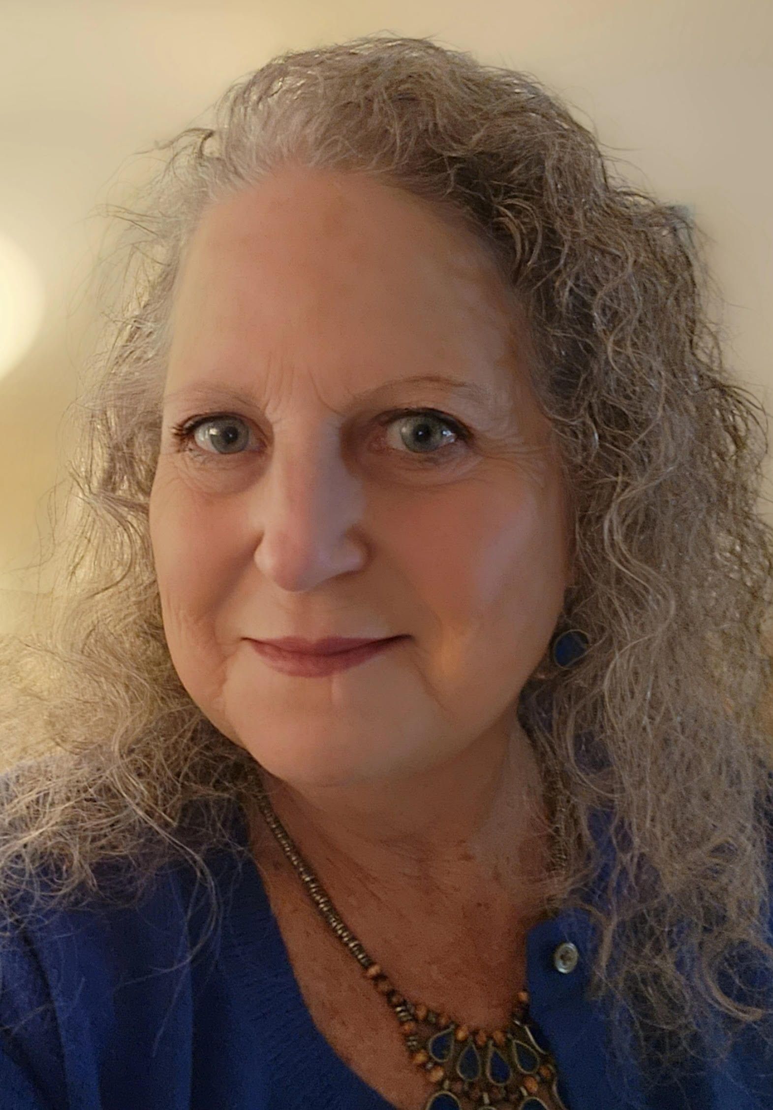 Woman with curly gray hair, smiling in a blue sweater.