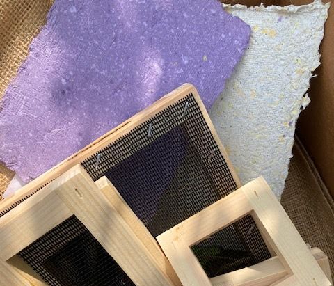 Wooden paper-making frames and colorful handmade paper sheets: purple, white, and textured.
