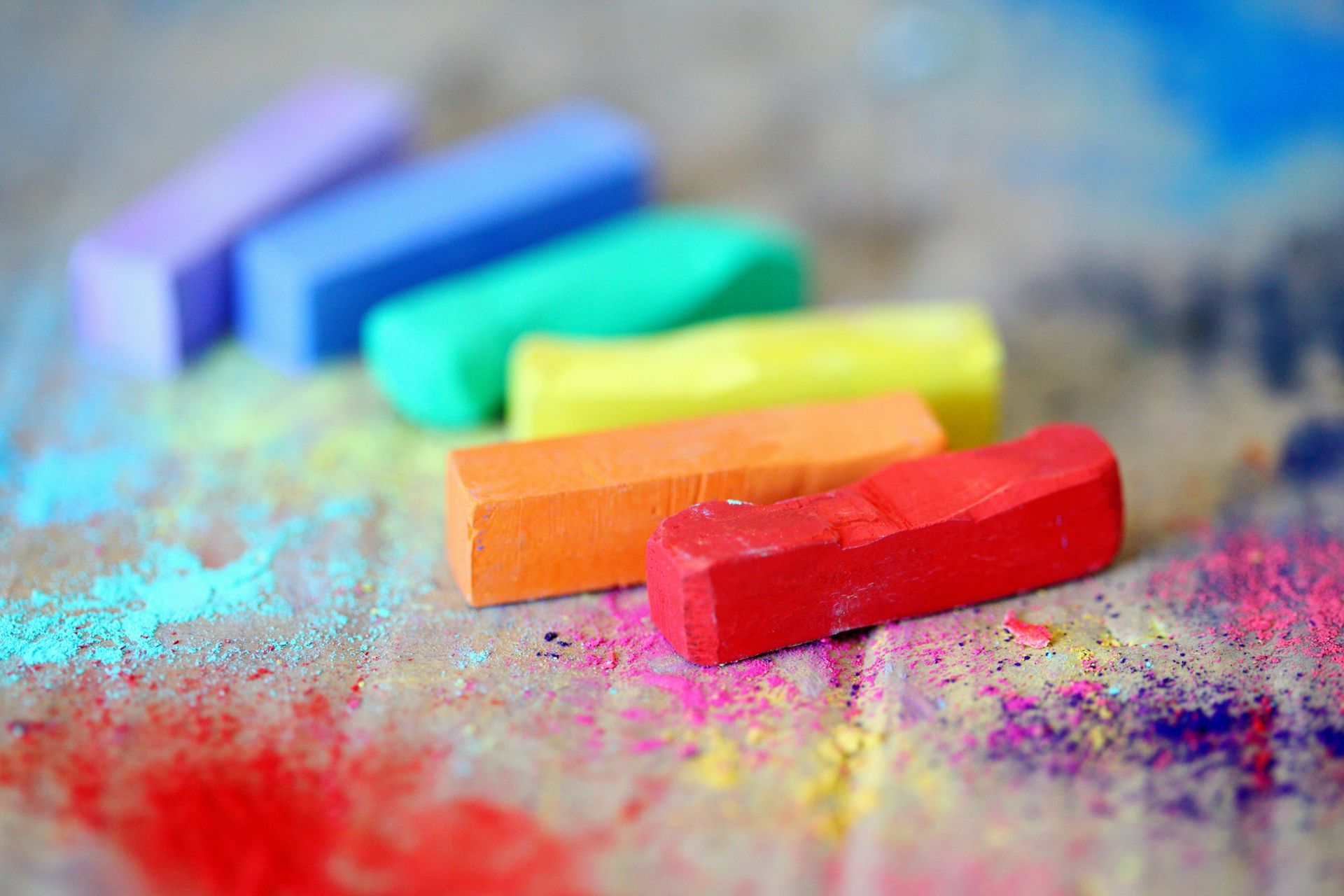 Colorful chalk sticks arranged in a row on a surface with scattered chalk dust.