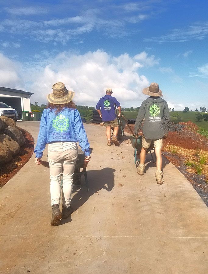 A Group of People Are Walking Down a Sidewalk Carrying Wheelbarrows — Full Circle Landscaping in Ballina, NSW