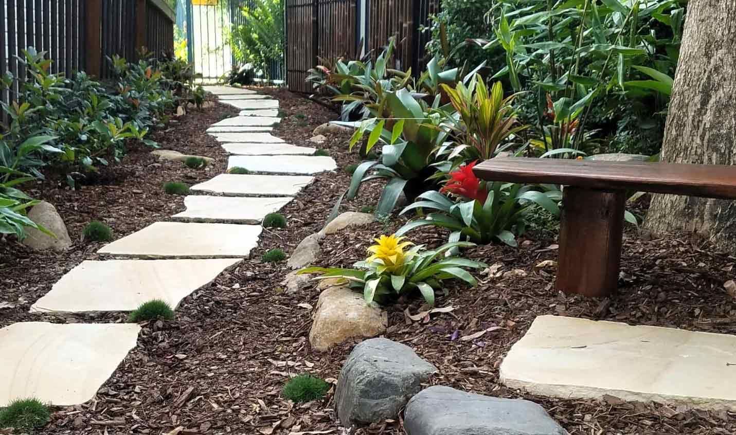 A Wooden Bench is Sitting on the Side of a Path in a Garden — Full Circle Landscaping in Tweed Heads, NSW