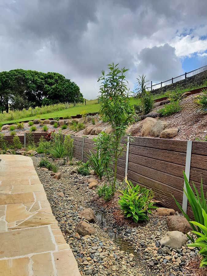A Stone Walkway Leading to a Lush Green Hillside With Trees and Rocks — Full Circle Landscaping in Murwillumbah, NSW