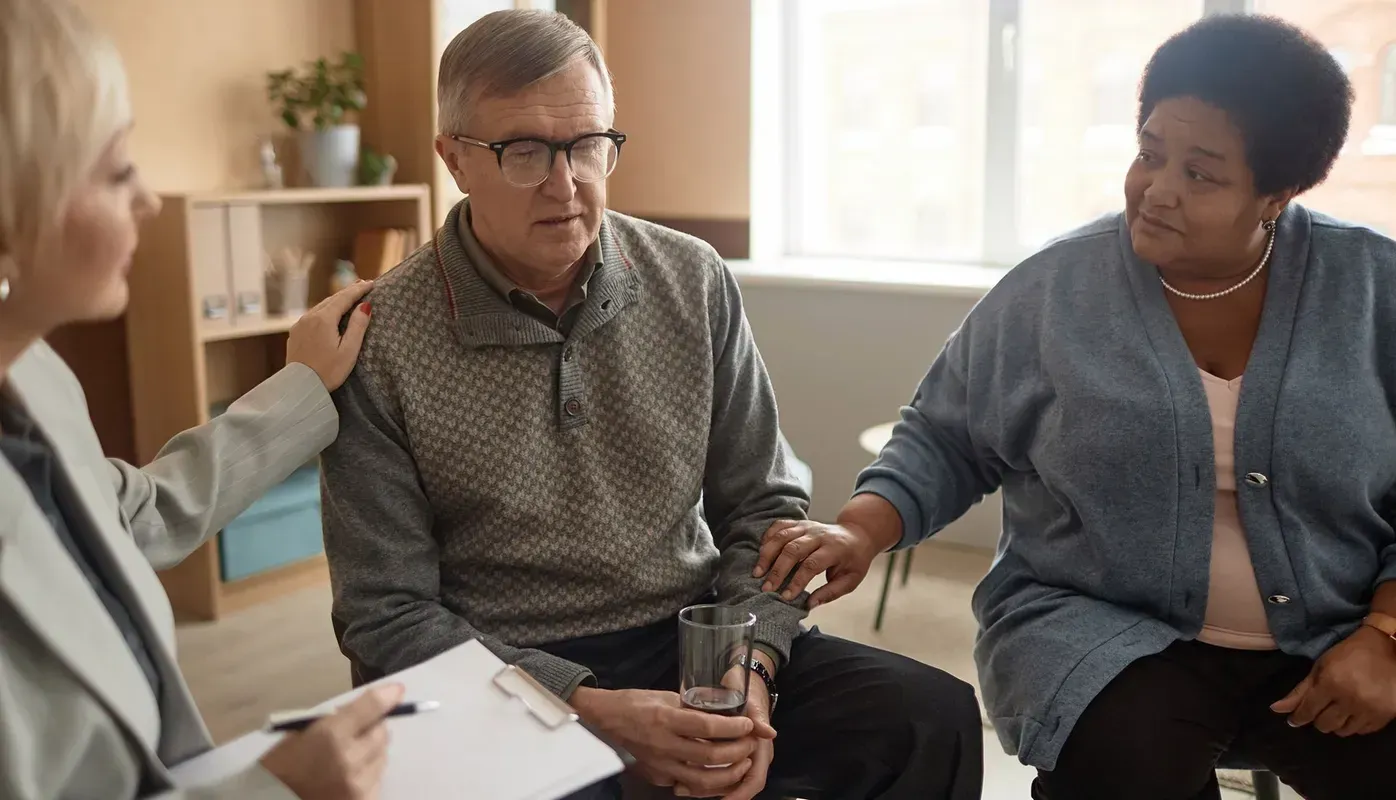 Three people in a counseling session; a man and woman comforted by a therapist.
