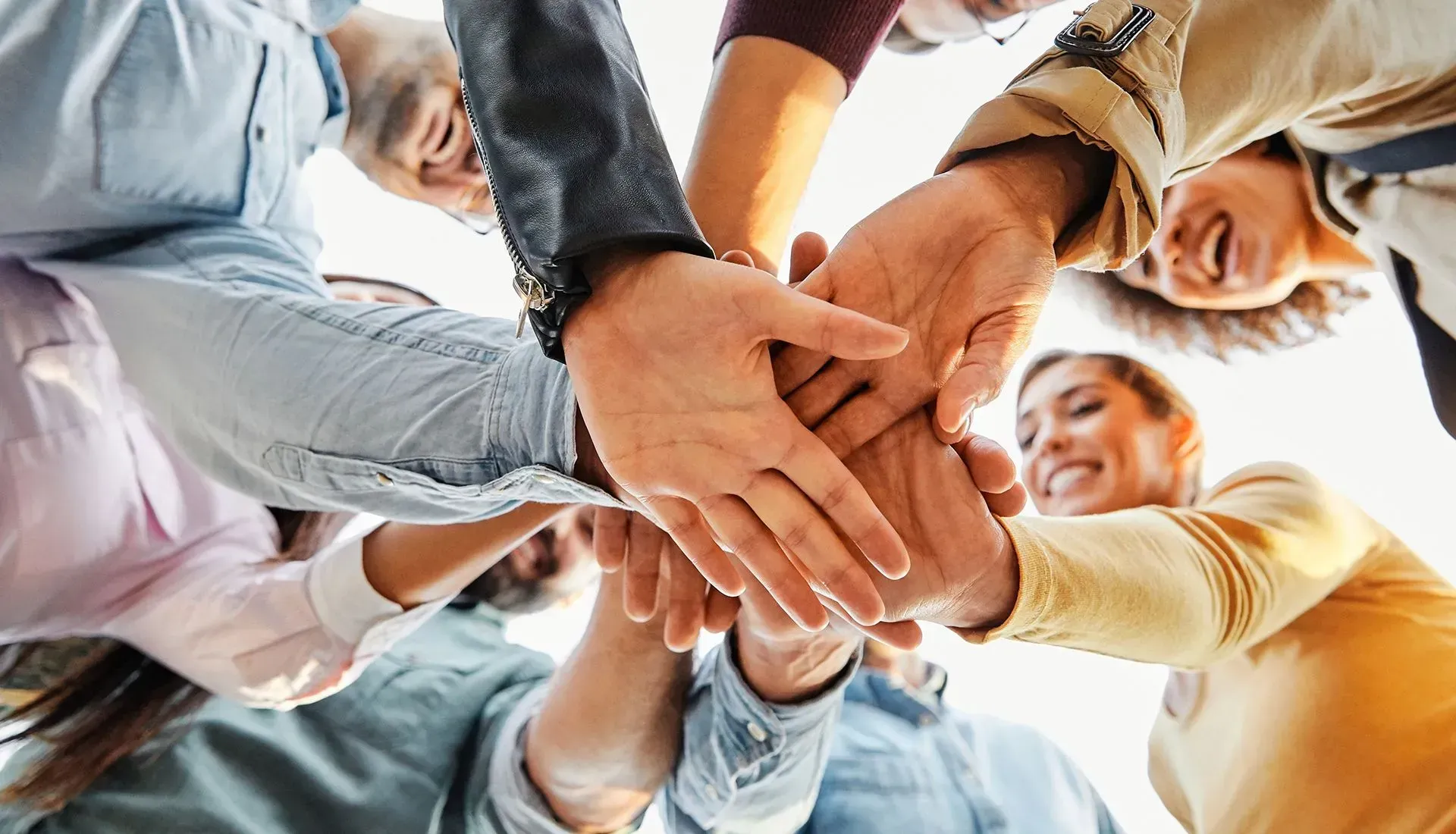 People with hands stacked together in a circle, smiling, viewed from below.
