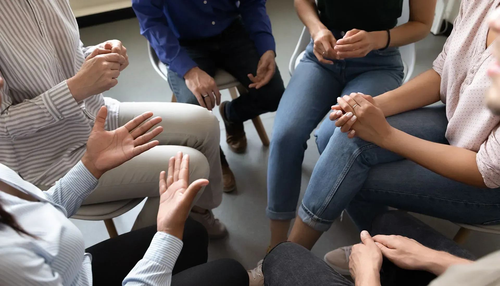 People in a circle, hands gesturing, engaged in a discussion; possibly group therapy or support meeting.
