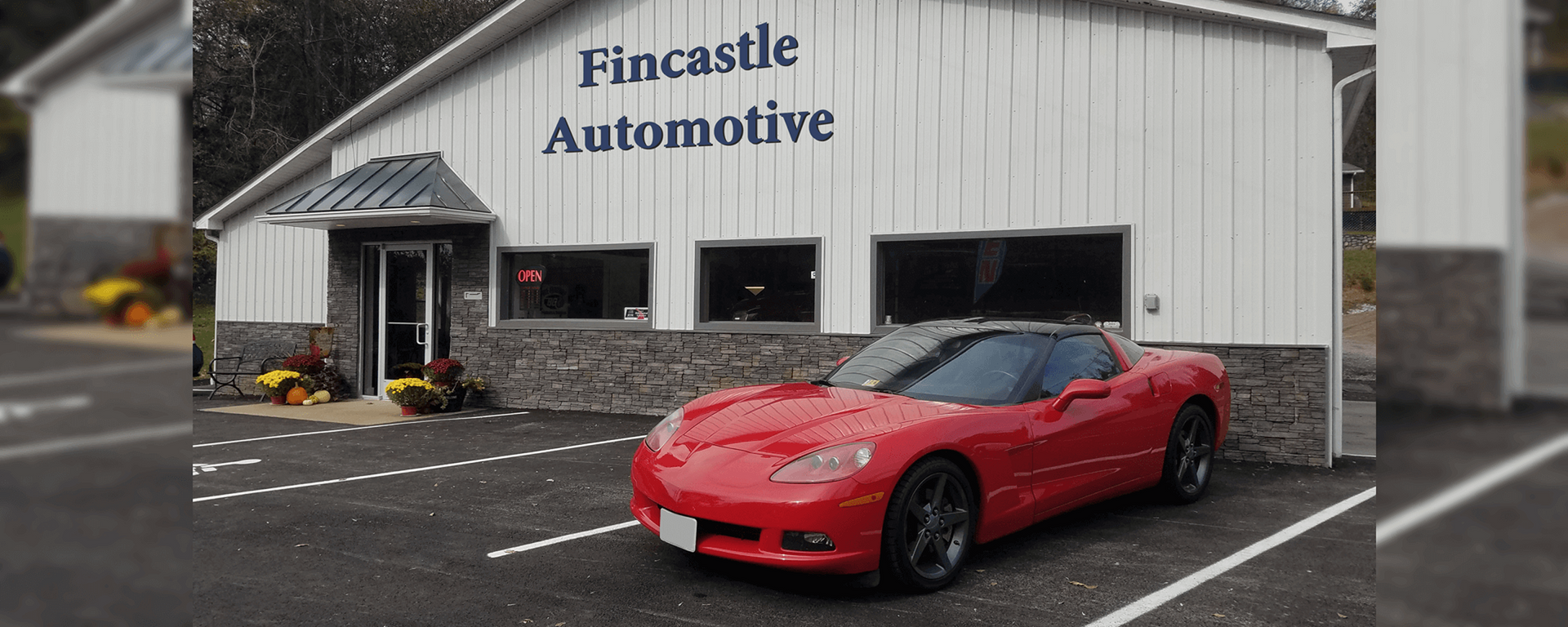 Red sports car parked in front of Fincastle Automotive shop, with white building and blue sign. | Fincastle Automotive