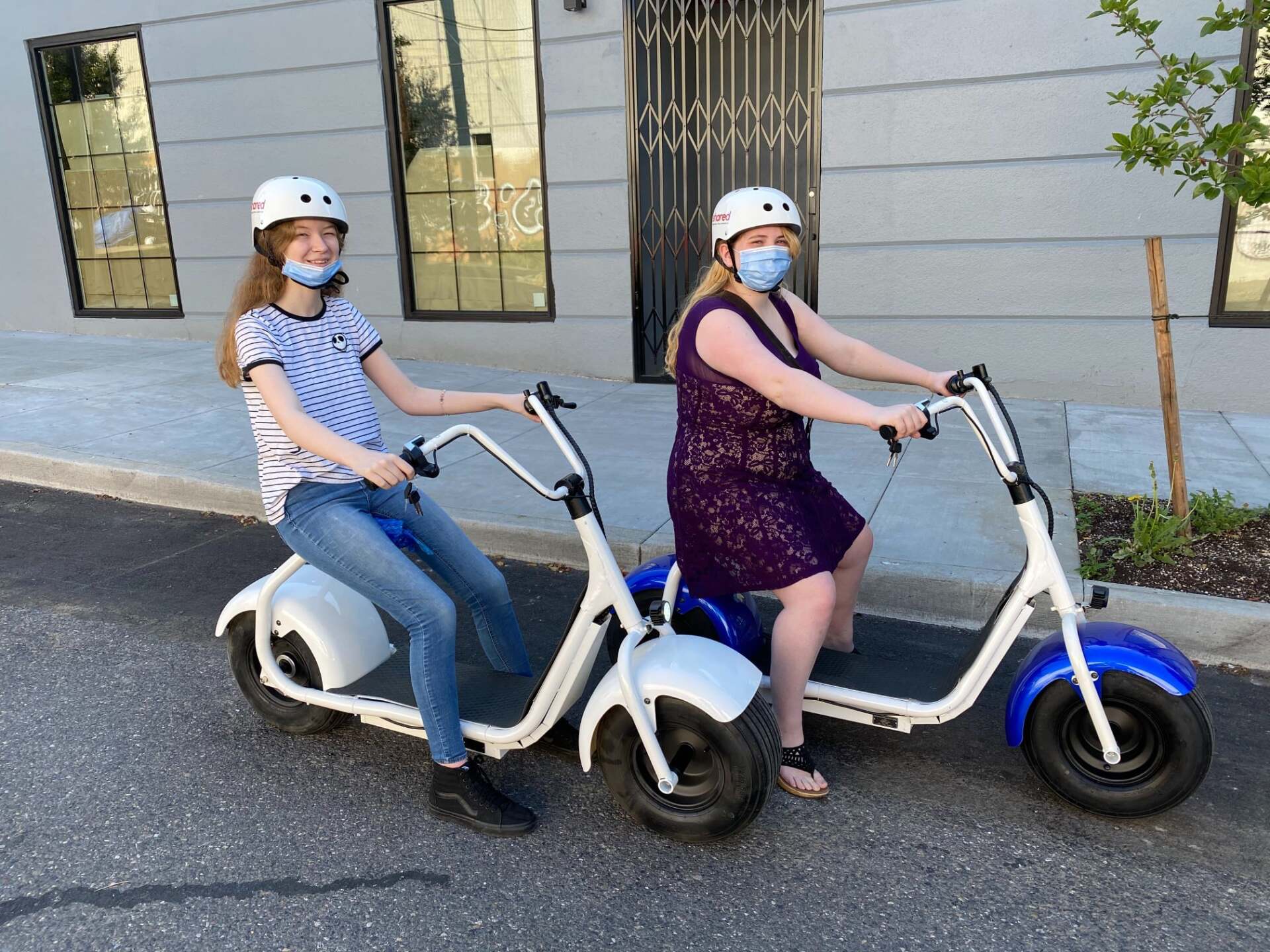 two women wearing masks are riding scooters on the street