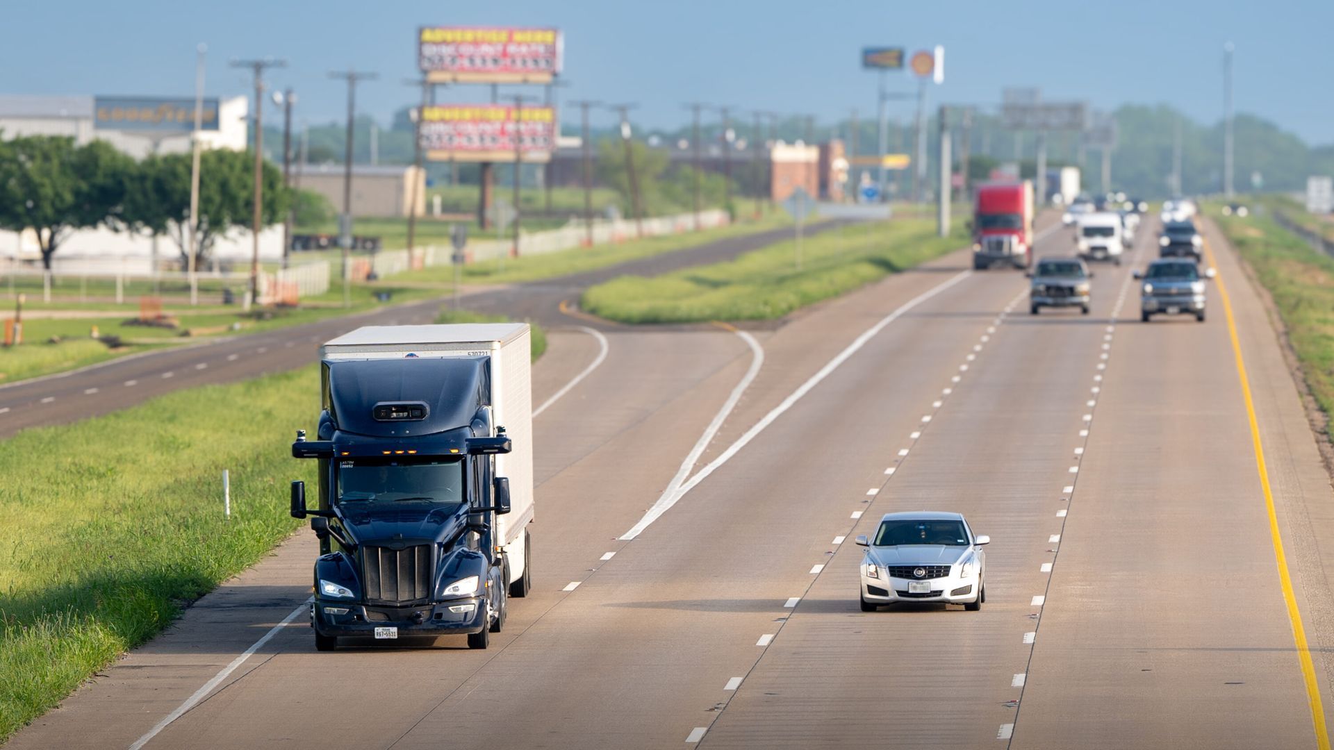 A semi truck is driving down a Dallas TX  highway next to a car.