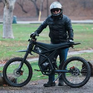 A man wearing a helmet is standing next to a GT73 electric dirt bike.