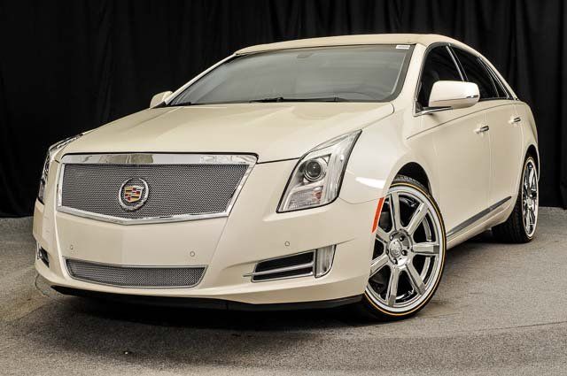 a white cadillac ats is parked in front of a black curtain .