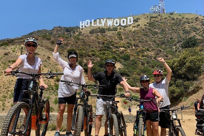 A group of people standing next to each other on bicycles in front of the hollywood sign.