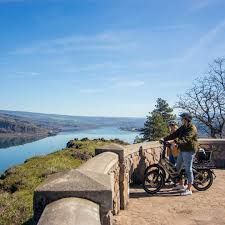 A man and a woman are standing next to a bicycle on top of a hill overlooking a river in Portland OR