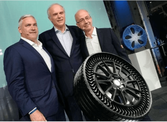 three men in suits standing next to a large tire