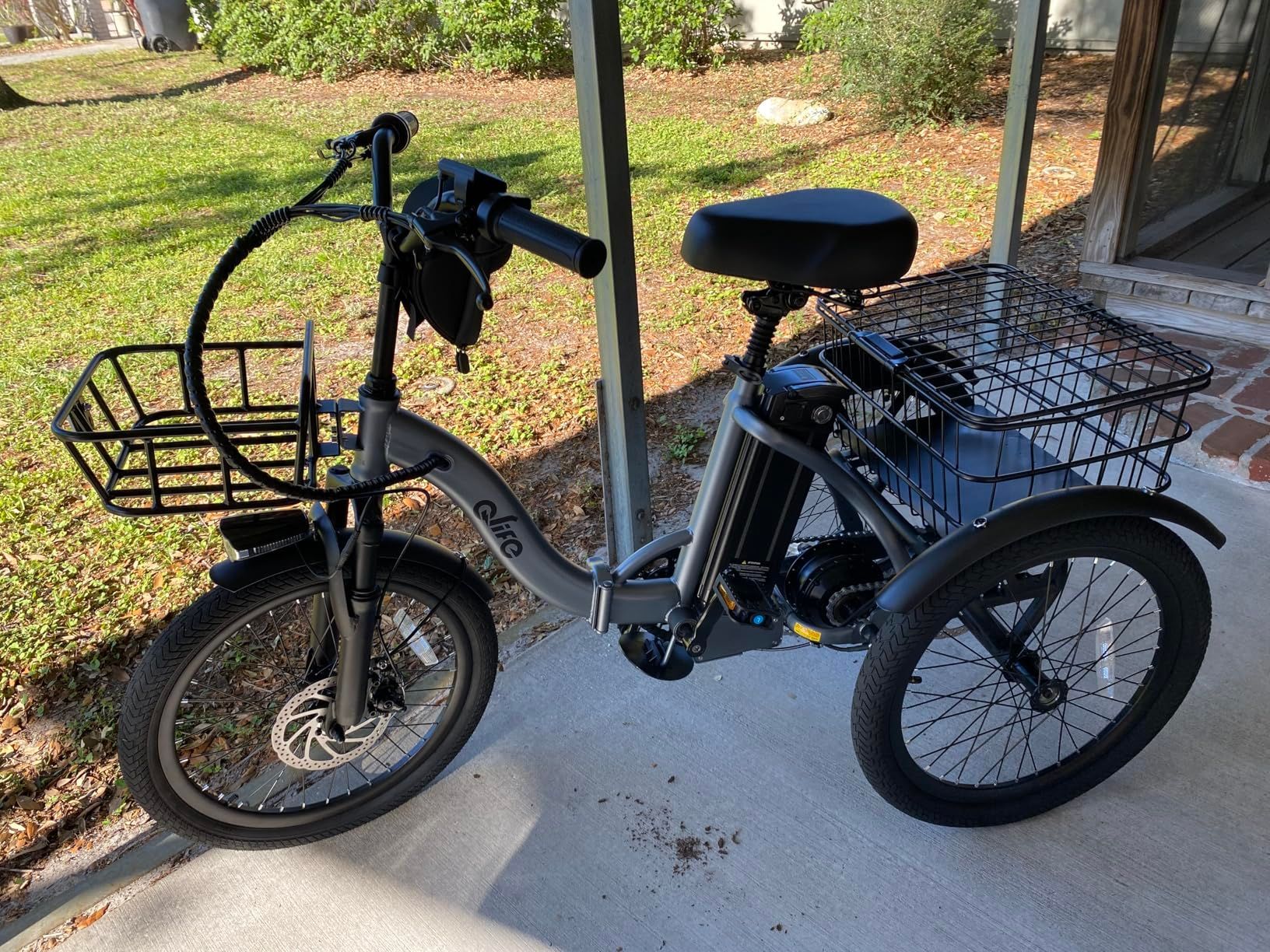 An electric Q TRACKER tricycle with a basket on the front is parked on a sidewalk.