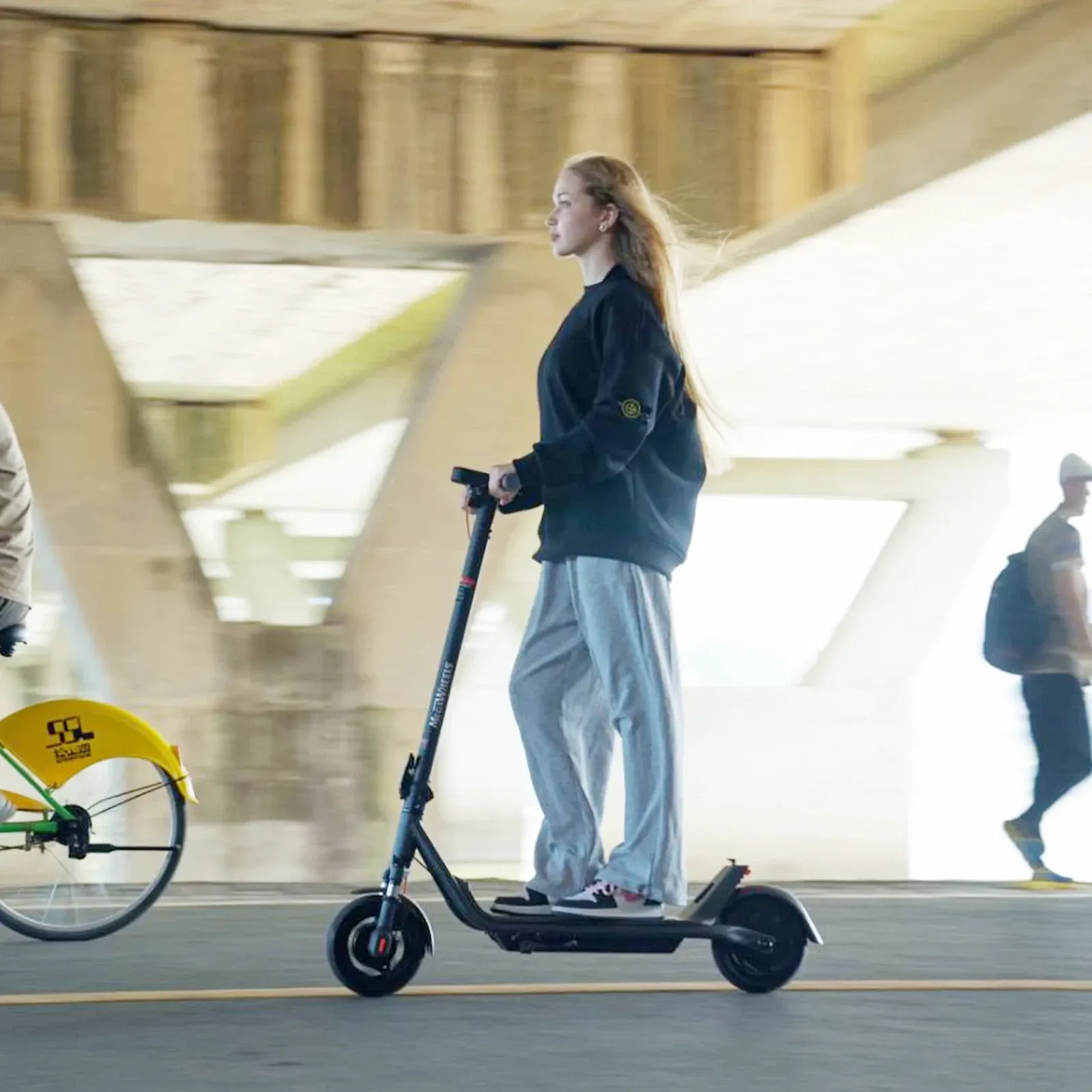 A woman is riding a TD PRO E-scooter under a bridge