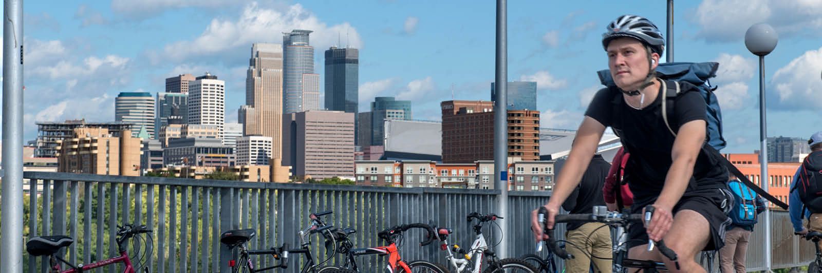 A man is riding a bike on a bridge with the Minneapolis, MN  city skyline in the background.
