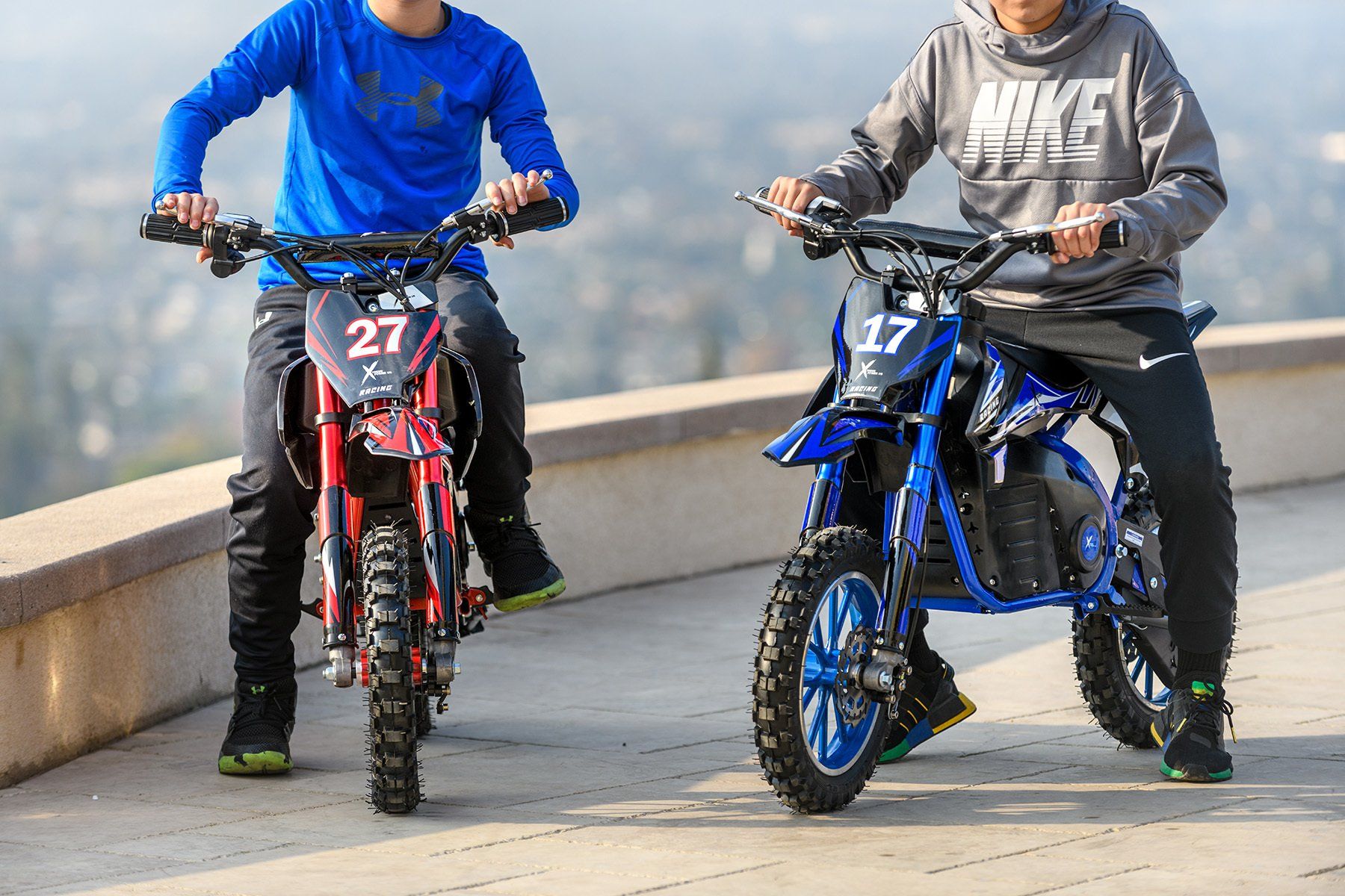 two young boys are riding dirt bikes on a sidewalk .