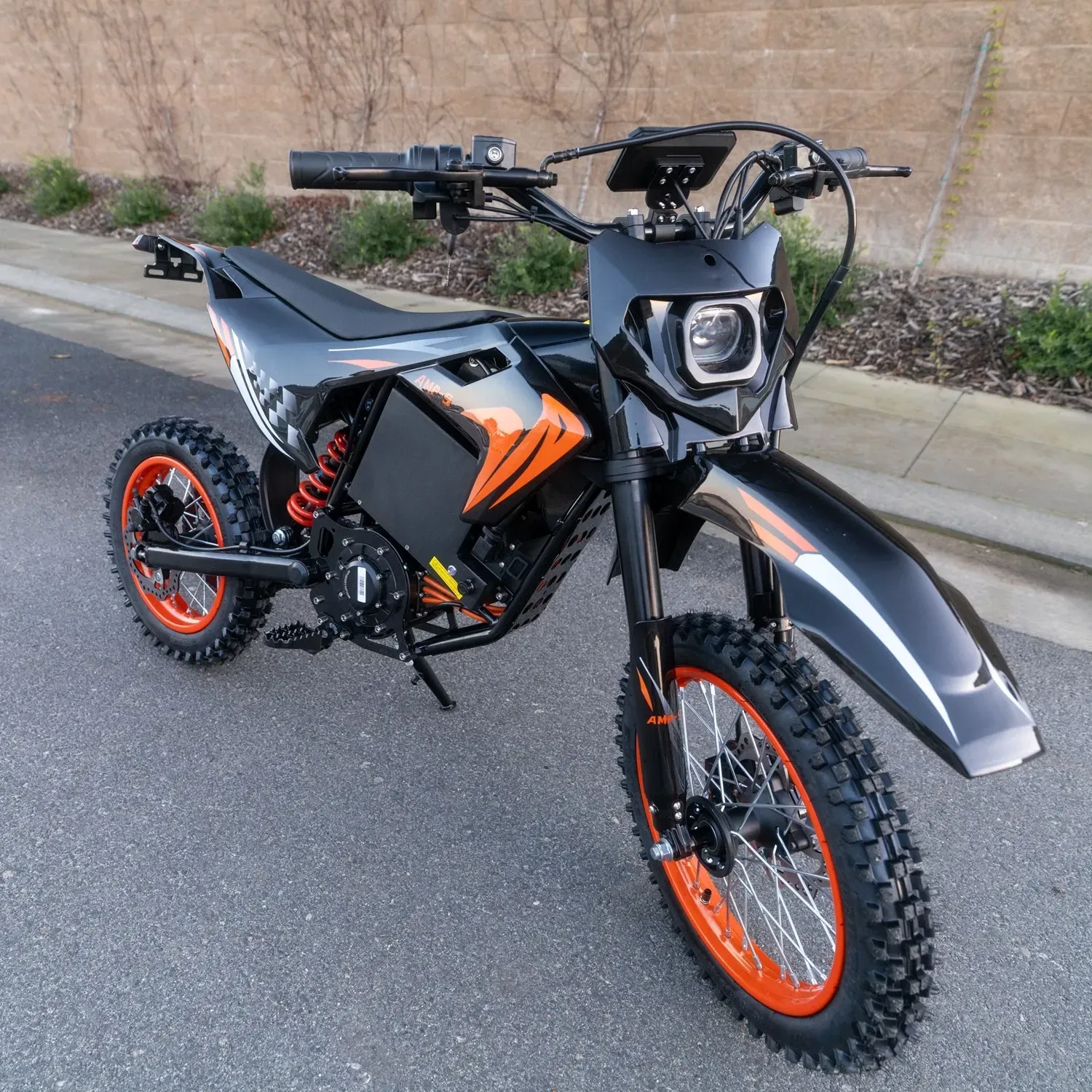 A black and orange electric dirt bike parked on an asphalt surface.