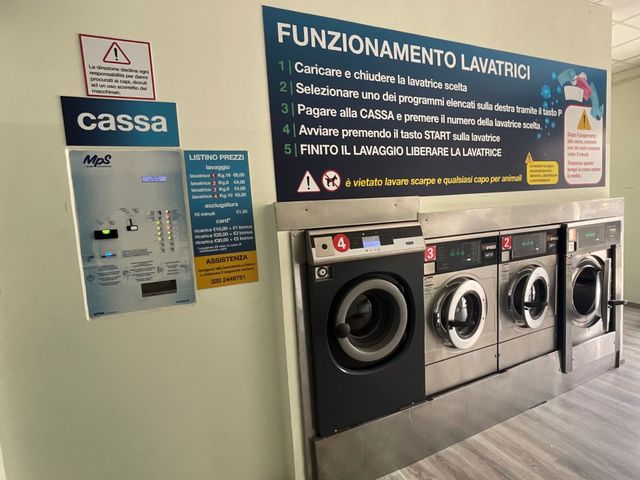 Lavanderia con quattro lavatrici a carica frontale e istruzioni in italiano sulla parete.