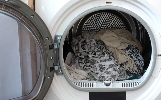 Asciugatrice aperta con una pila di vestiti all'interno, tra cui tessuti a fantasia e asciugamani.